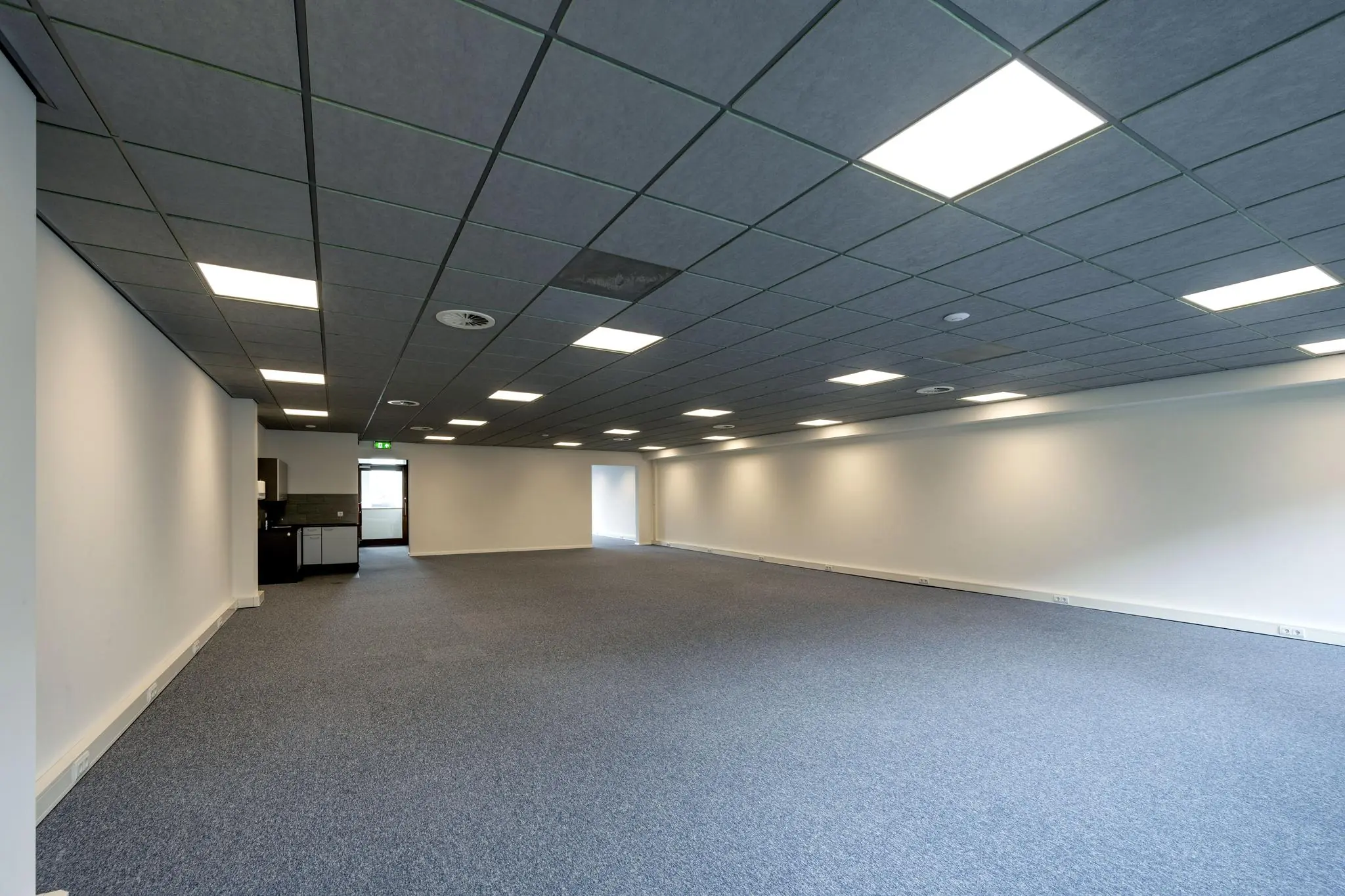 Leeg kantoorruimte met systeemplafond, tapijtvloer en een kitchenette aan de De Ruijterkade.